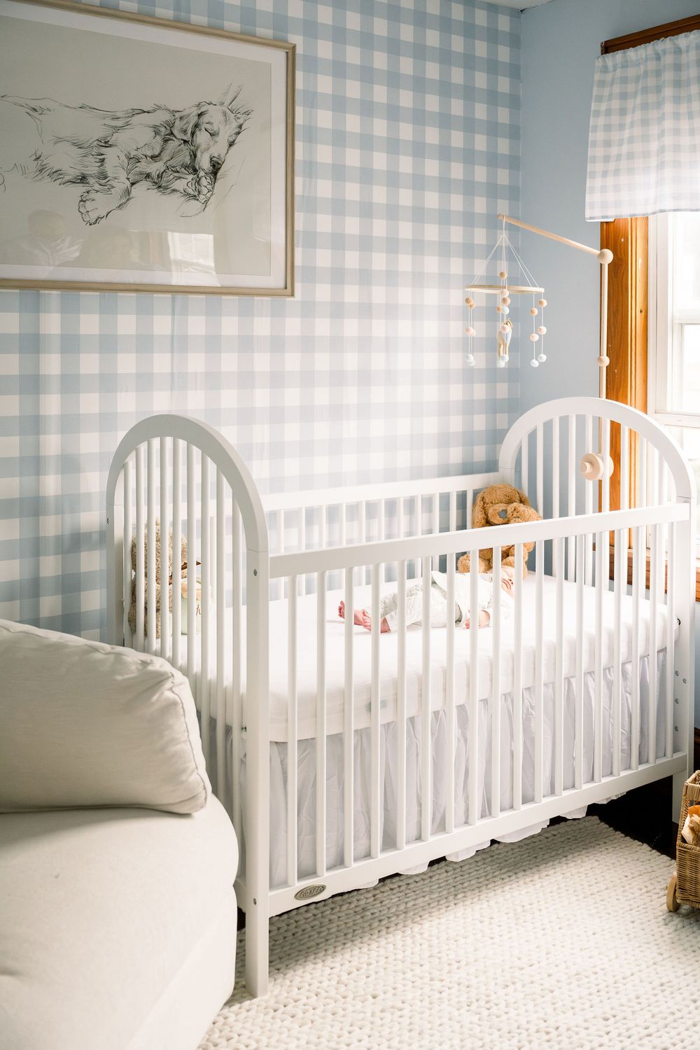 White crib in a nursery with light blue gingham wallpaper and white carpeting creates a serene baby room setting.