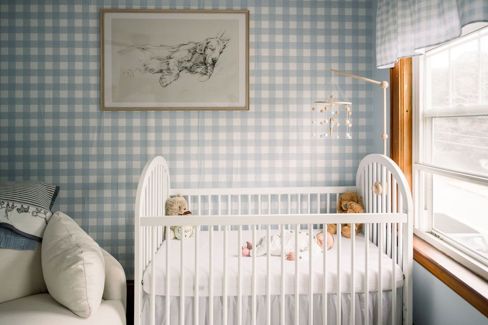 A cozy nursery room with blue gingham wallpaper, white crib, and natural light streaming through the window.