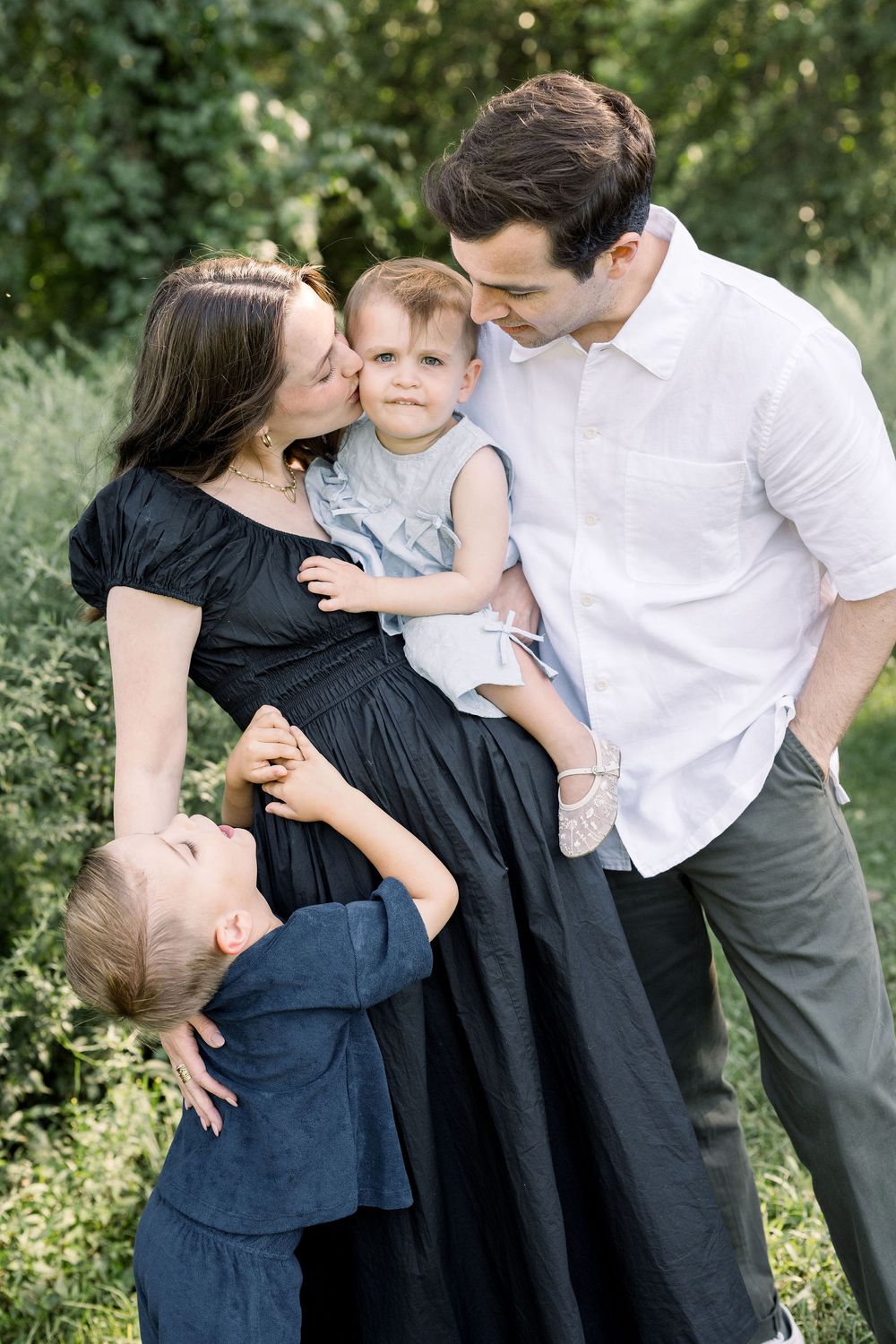 A family shares tender moments together in a series of candid outdoor portraits against a natural backdrop.