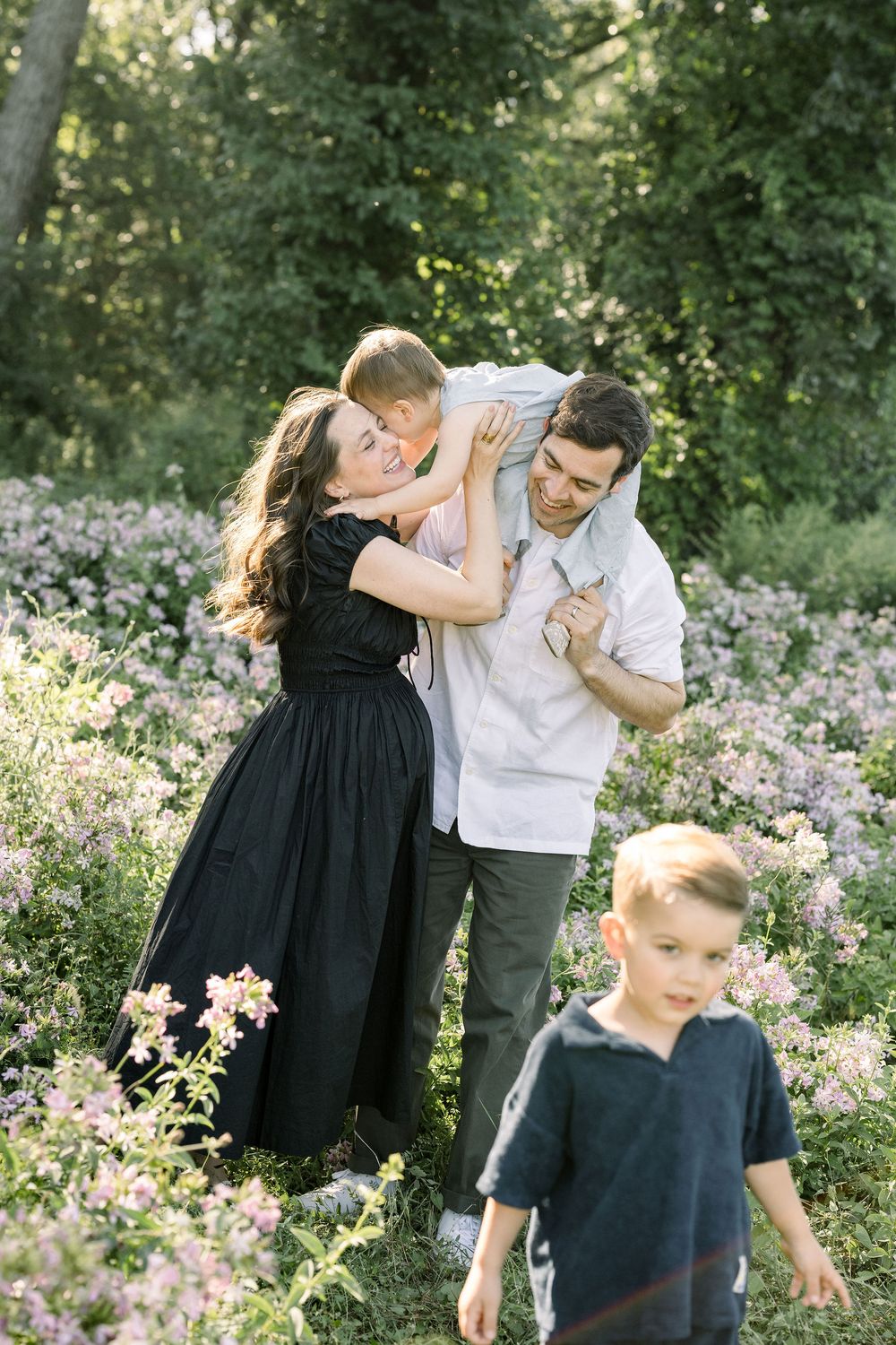 Family plays and embraces in a blooming wildflower field during a summer photo session.