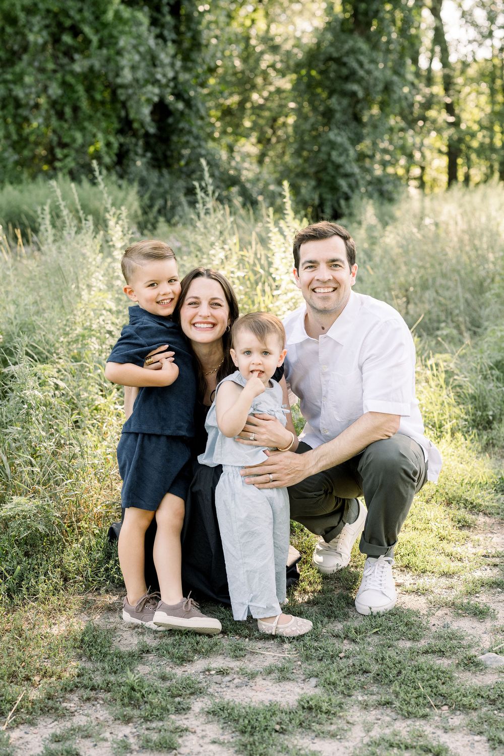 Candid family photos showing playful interactions between parents and children on grassy ground with trees in background.