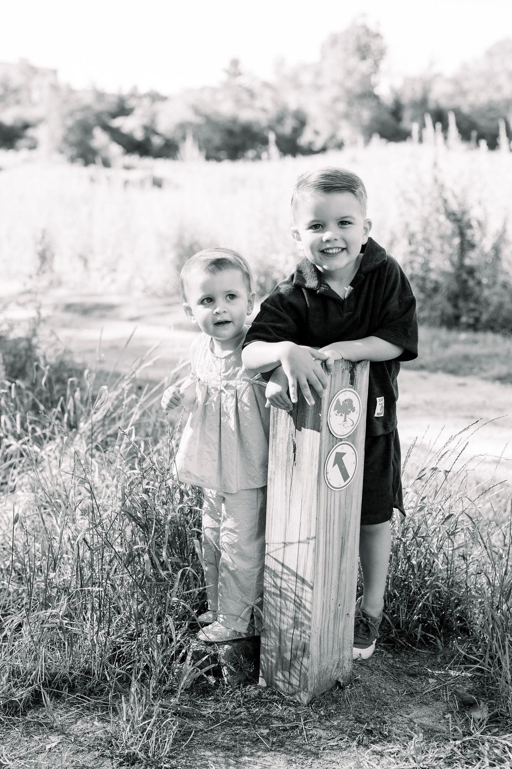 Black and white portrait series showing playful interactions near a rustic wooden fence in a grassy field.