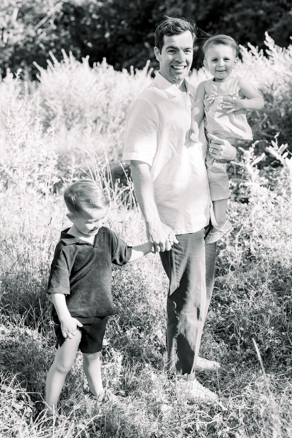 Candid outdoor family moments captured in a sunlit meadow with tall grass and natural surroundings.