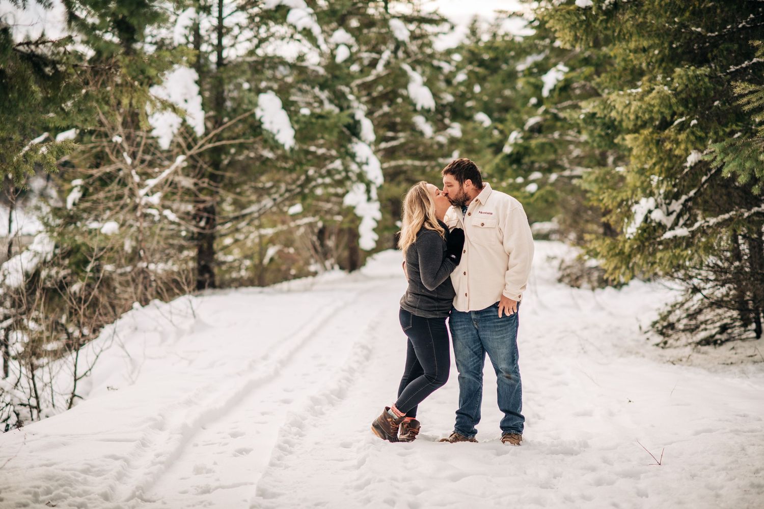 A couple shares romantic moments in a snowy winter forest setting during an outdoor photo session.