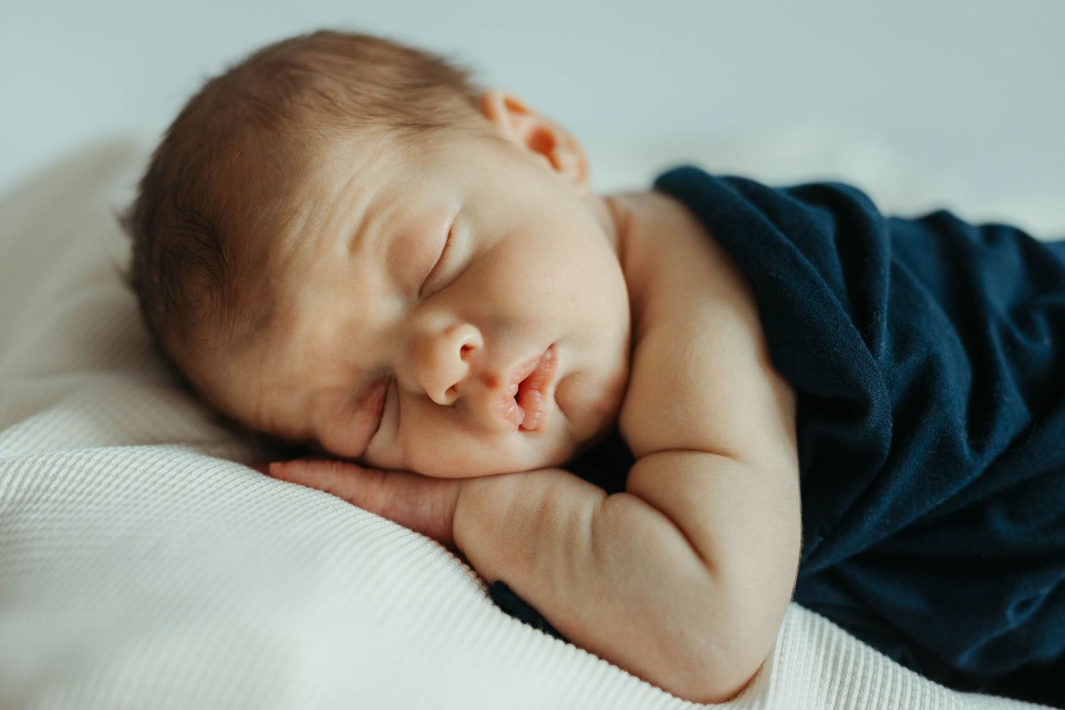 Peaceful sleeping newborn wrapped in navy blue blanket during studio session.