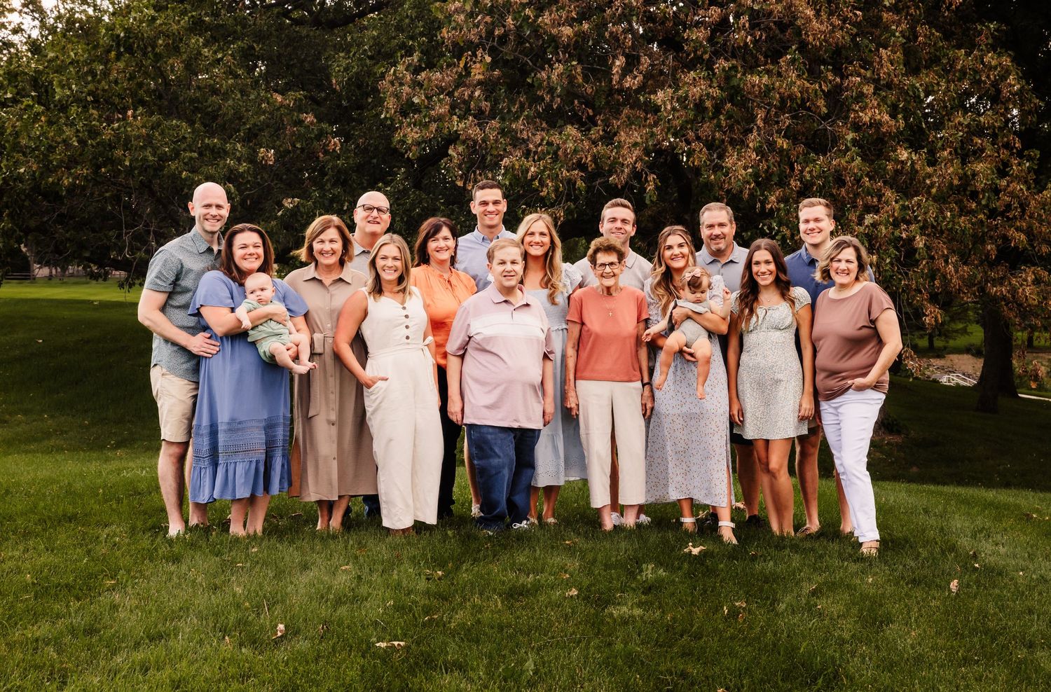 Large family group poses together outdoors under autumn trees at sunset.