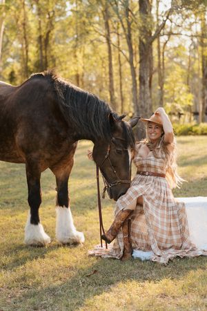 A Shire horse with feathered hooves stands beside someone in a plaid dress during a golden sunset photoshoot in Sydney