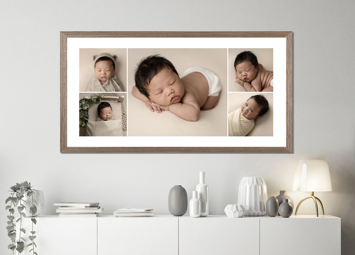 Elegant newborn photography studio setup with framed portraits and white furniture against a neutral wall.