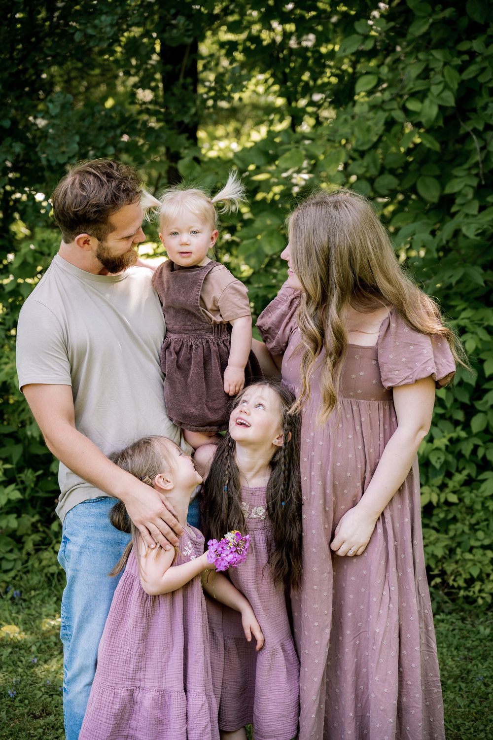 Family wearing coordinating purple and mauve outfits share tender moments together in a garden setting.