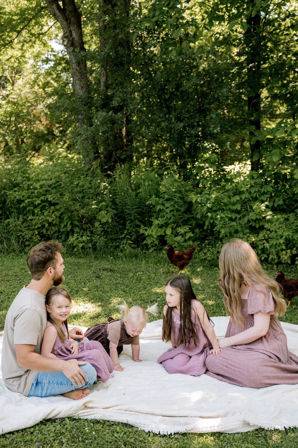 Family lying together on white blanket in park having intimate moment under trees.