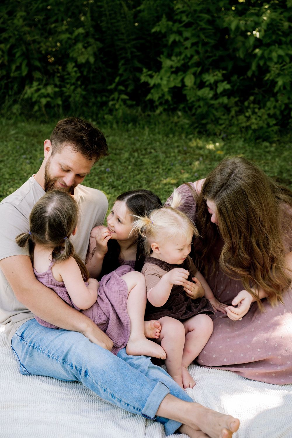 A family shares an intimate moment together while relaxing on a blanket in a green outdoor setting.
