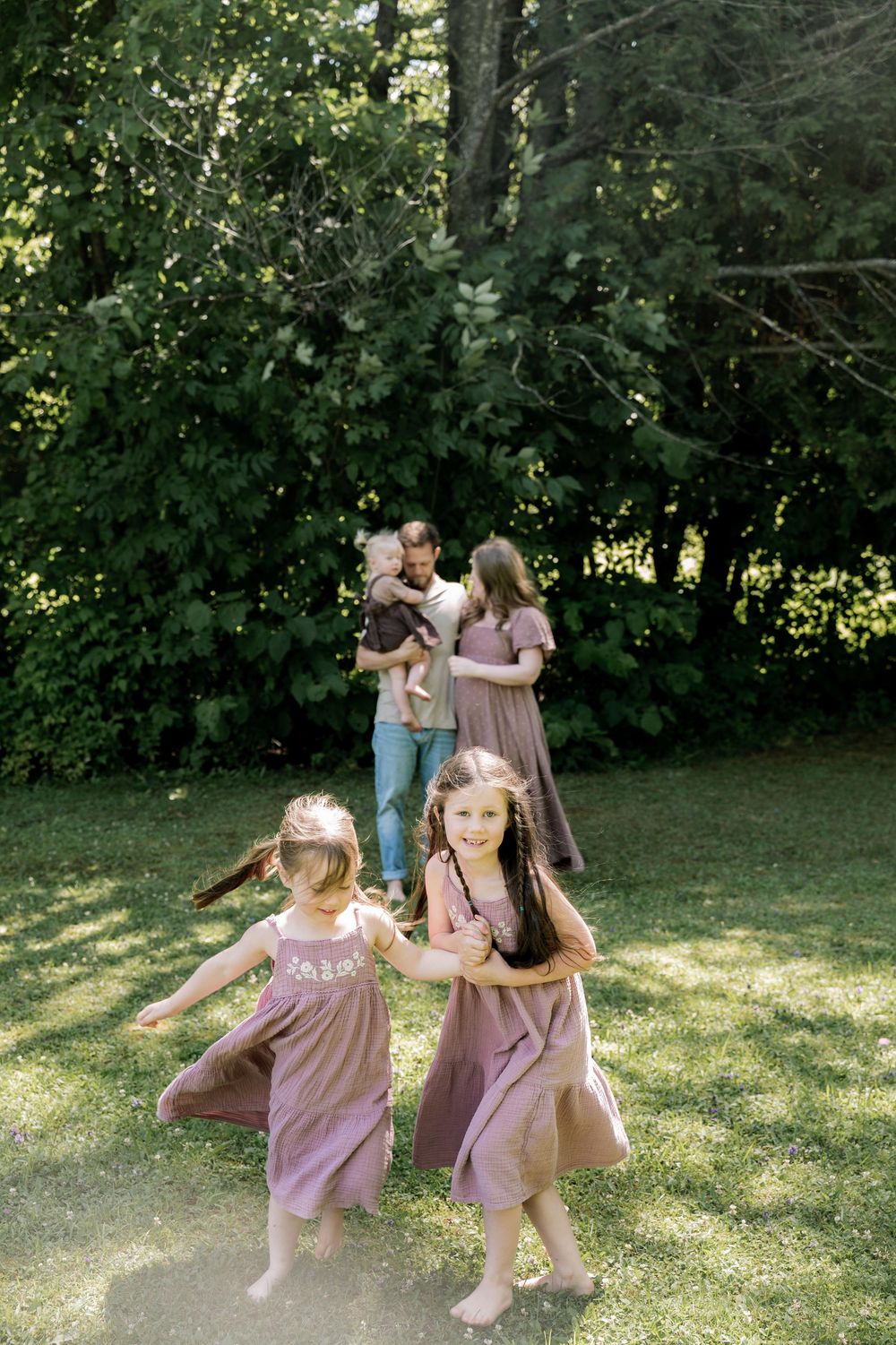 Children in matching pink dresses dance and play together in a sunlit garden setting.