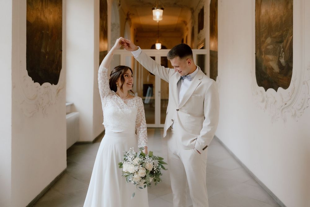 Elegant wedding couple poses in a white corridor with ornate walls and vintage decor.