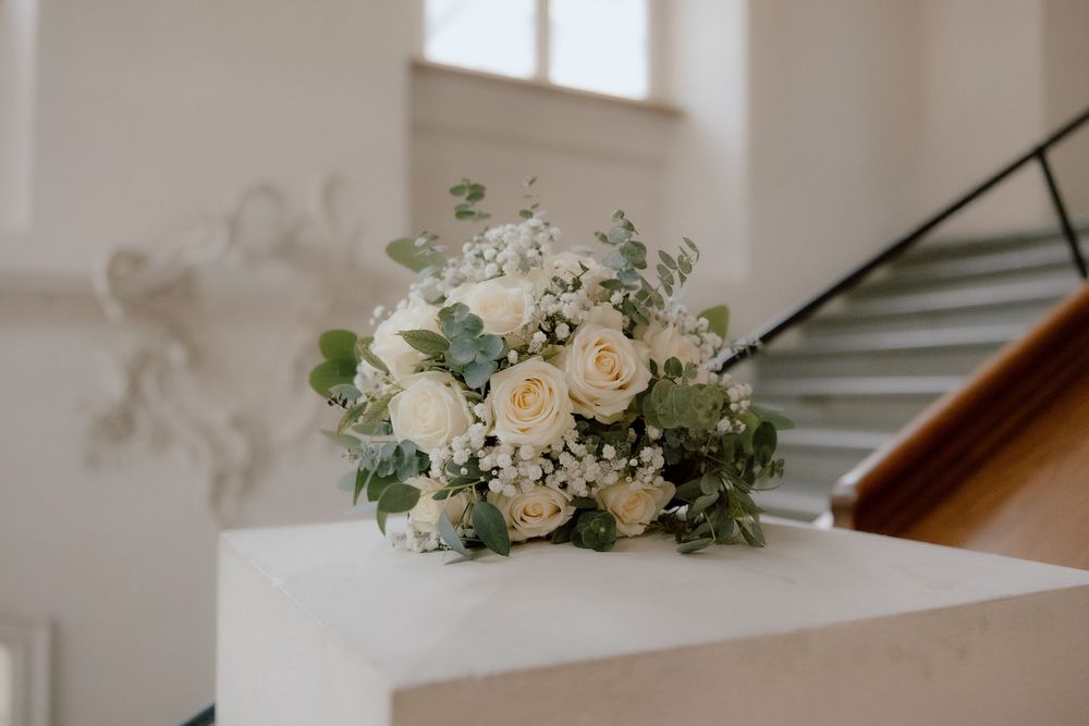 White roses and delicate greenery arranged in an elegant floral wedding decoration on a wooden surface.