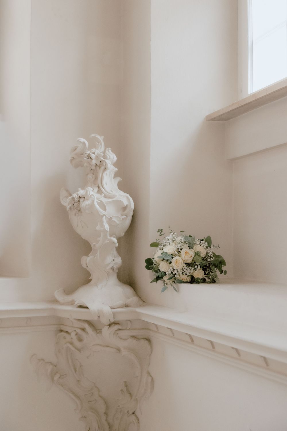White decorative plaster sculptures and fresh flowers adorn a windowsill in an elegant interior setting.