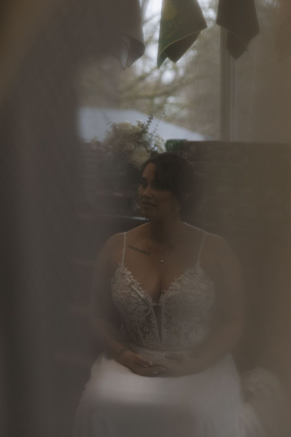 Dreamy soft-focus portrait of bride in lace wedding gown viewed through sheer curtains outdoors.