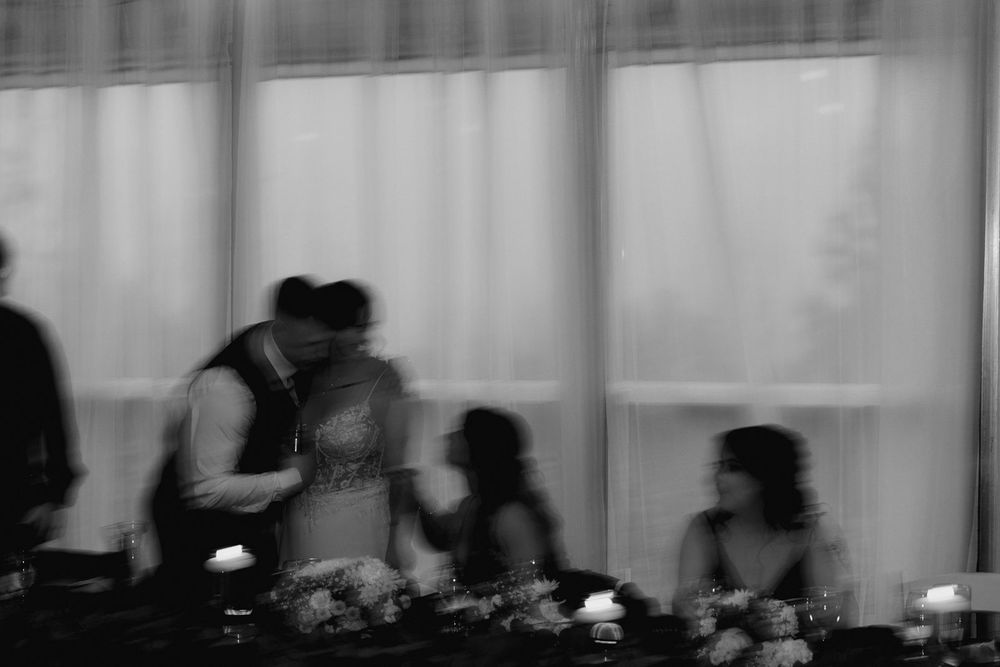 Blurred black and white photo of wedding guests mingling at a candlelit reception table.