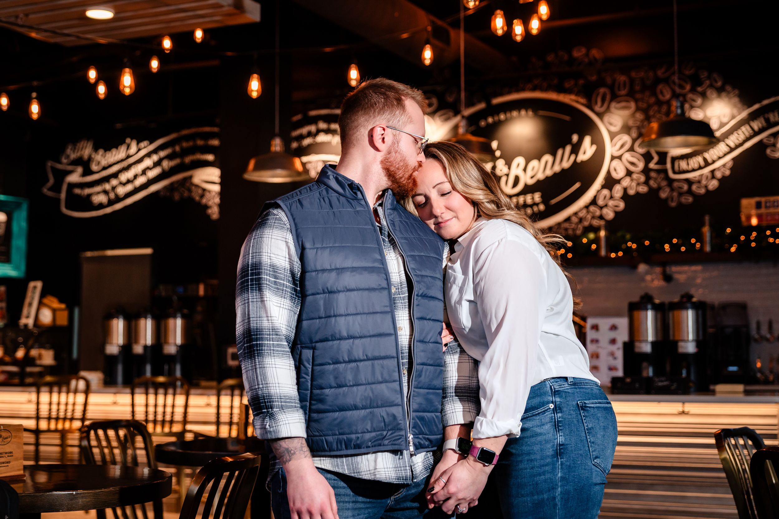 A couple embraces in a warmly lit restaurant with decorative lights in the background.