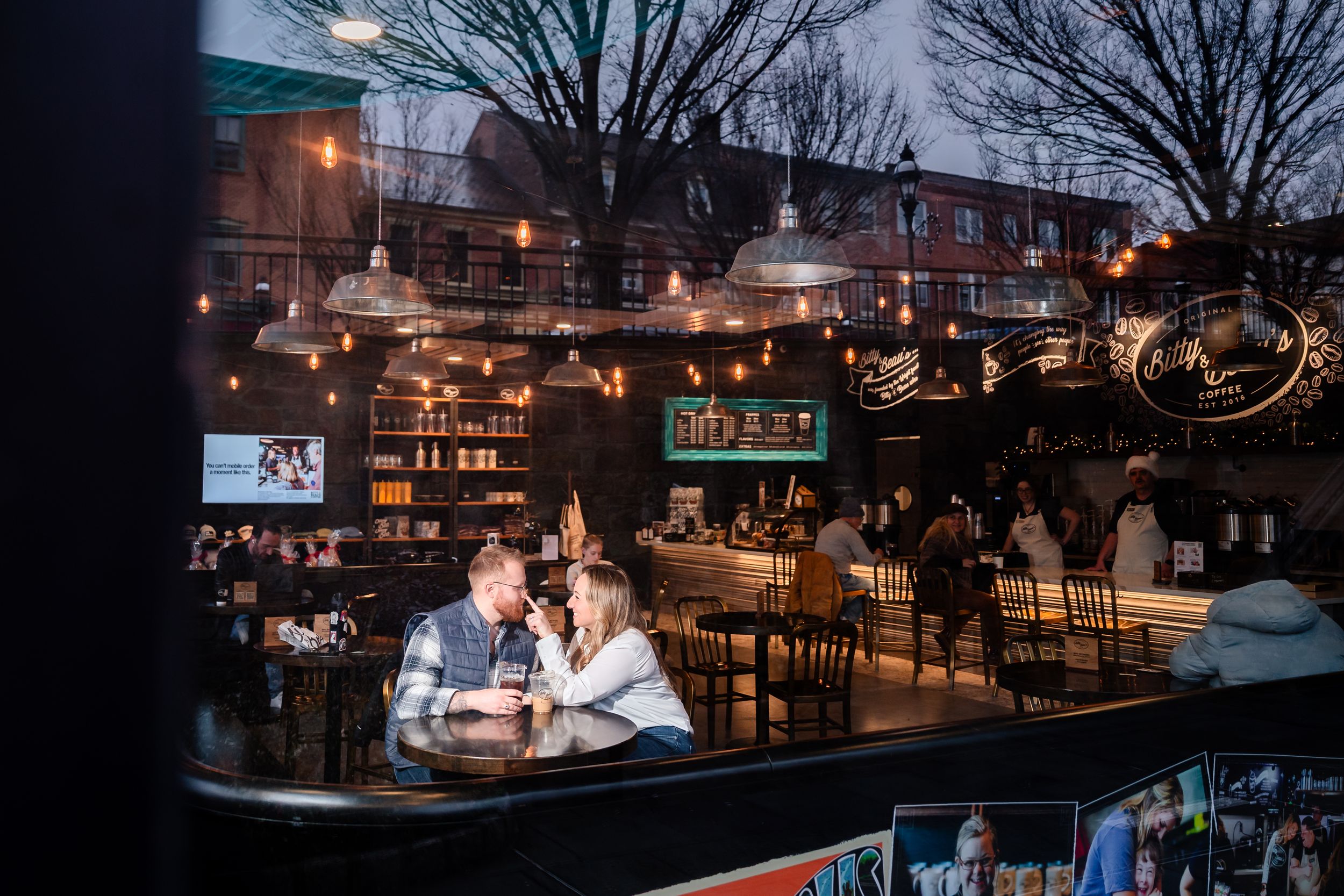 Cozy restaurant interior with string lights and winter scenery visible through large windows at dusk.