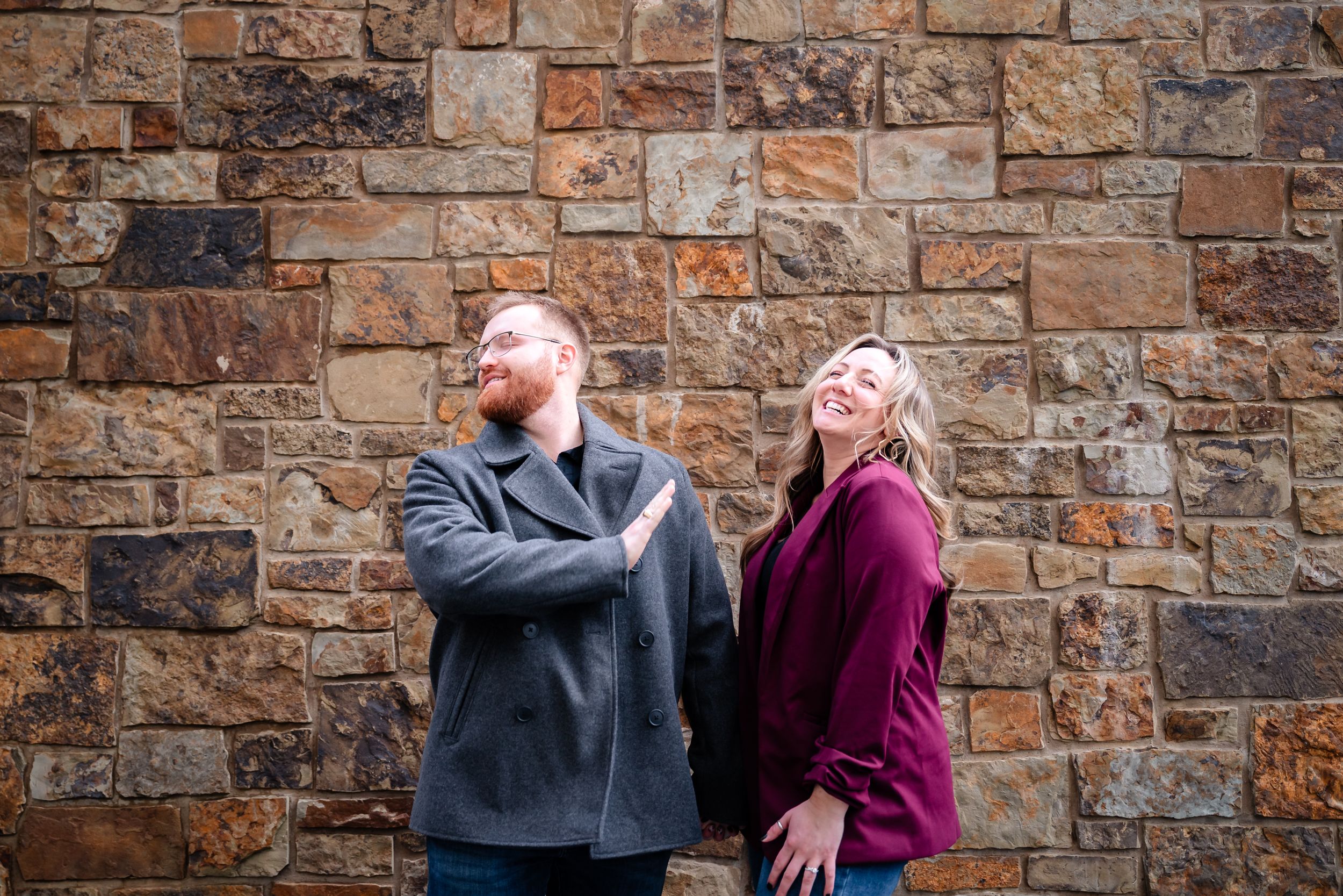 Couple embracing against rustic stone wall backdrop during romantic photoshoot.