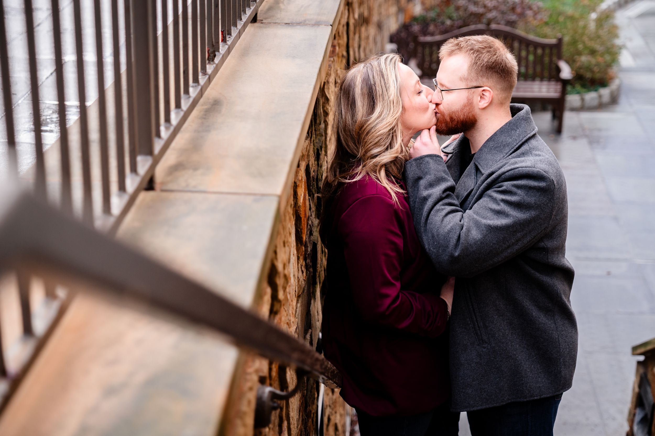 A couple shares an intimate moment while walking along an outdoor railing on an overcast day.