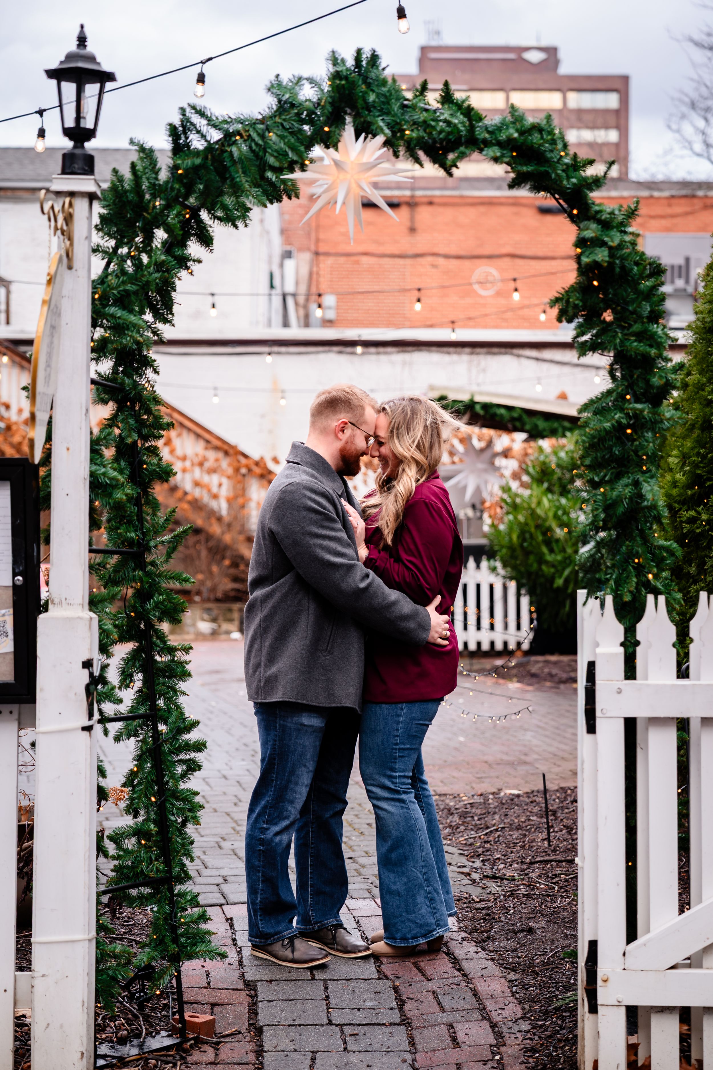 A couple shares intimate moments along a garden path with white picket fences and greenery.