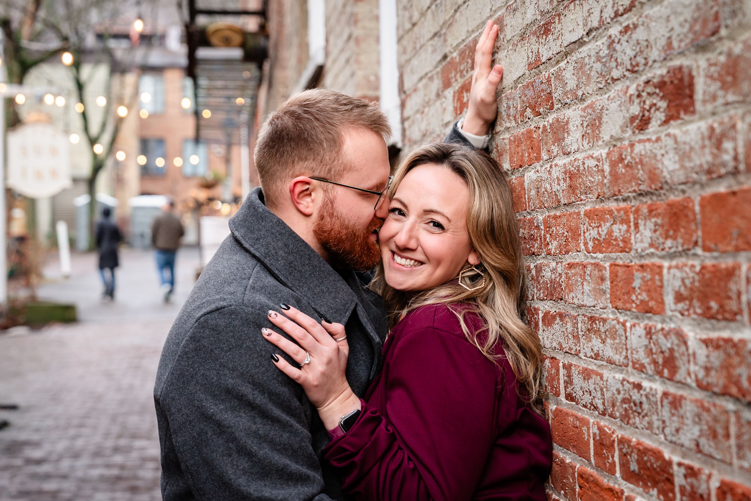 A romantic couple embraces against a rustic brick wall during an engagement photo session.