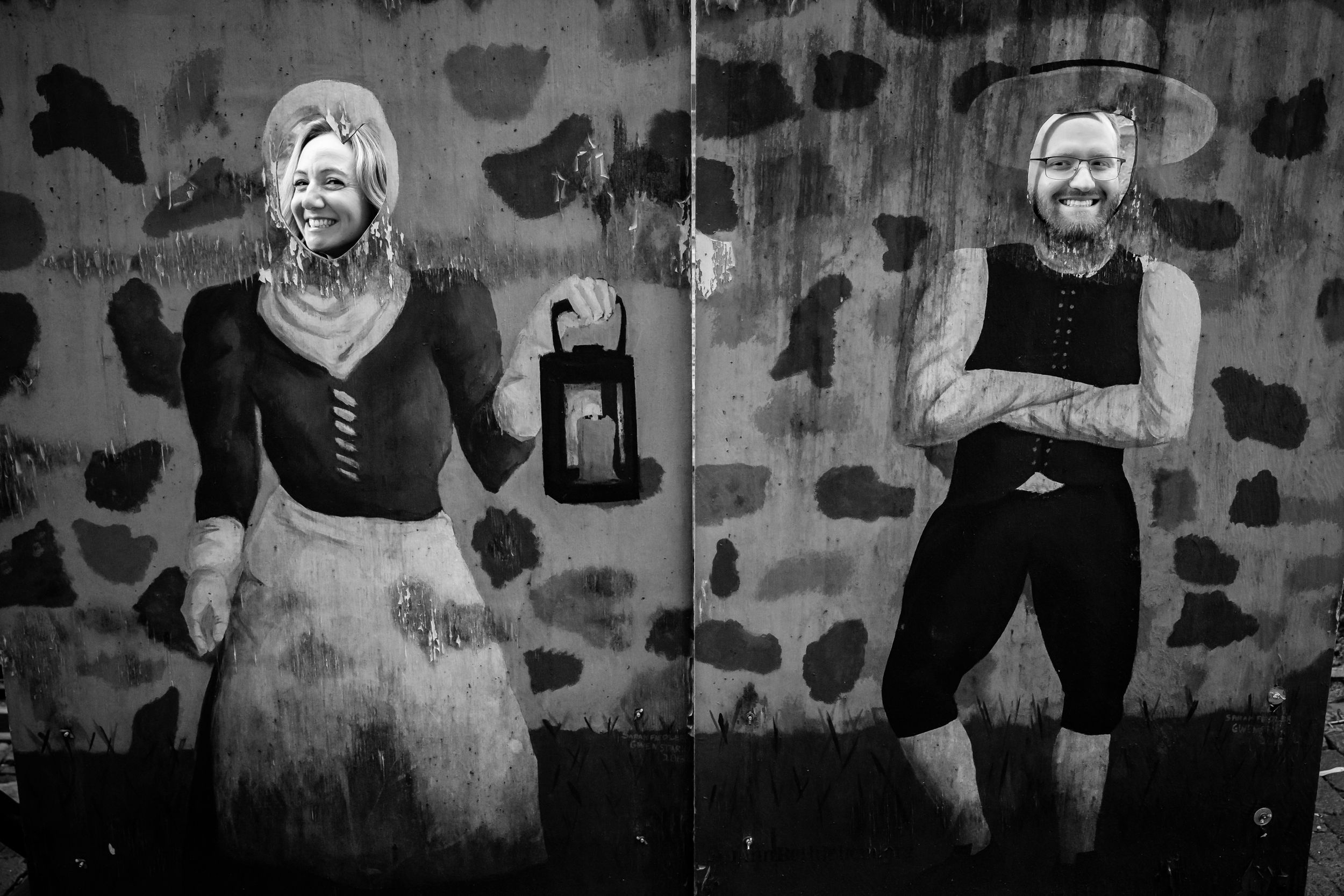 A black and white vintage photograph shows two people posing against a textured wall with a lantern decoration.