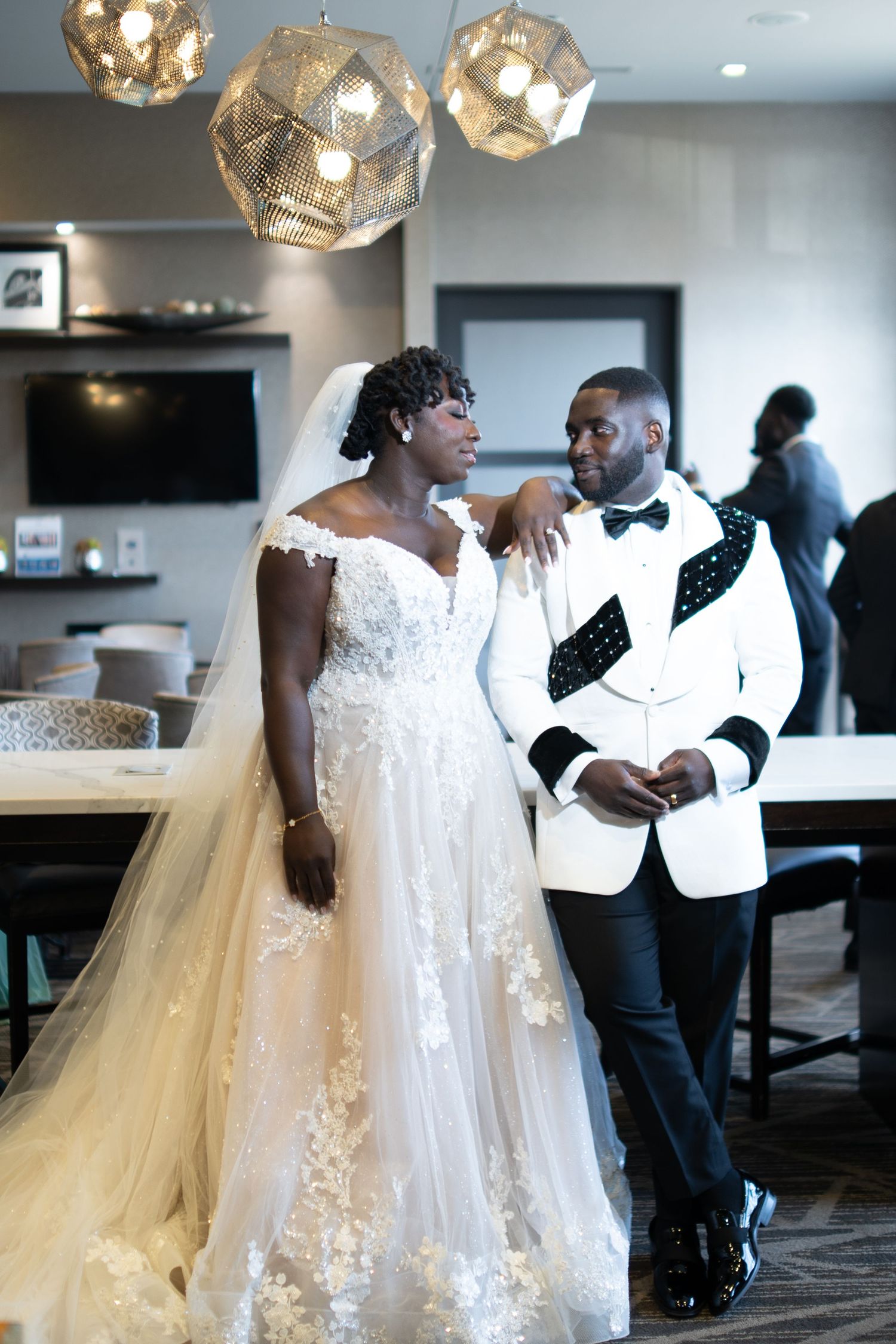 A couple shares an intimate moment at their wedding reception under elegant geometric pendant lights.