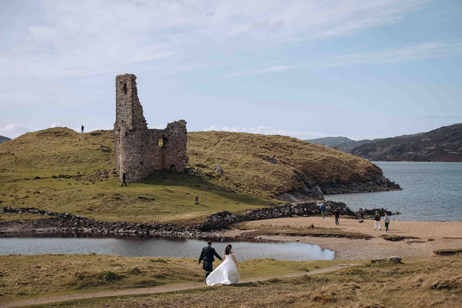 A scenic coastal landscape featuring ancient stone castle ruins overlooking a tranquil bay in Scotland.