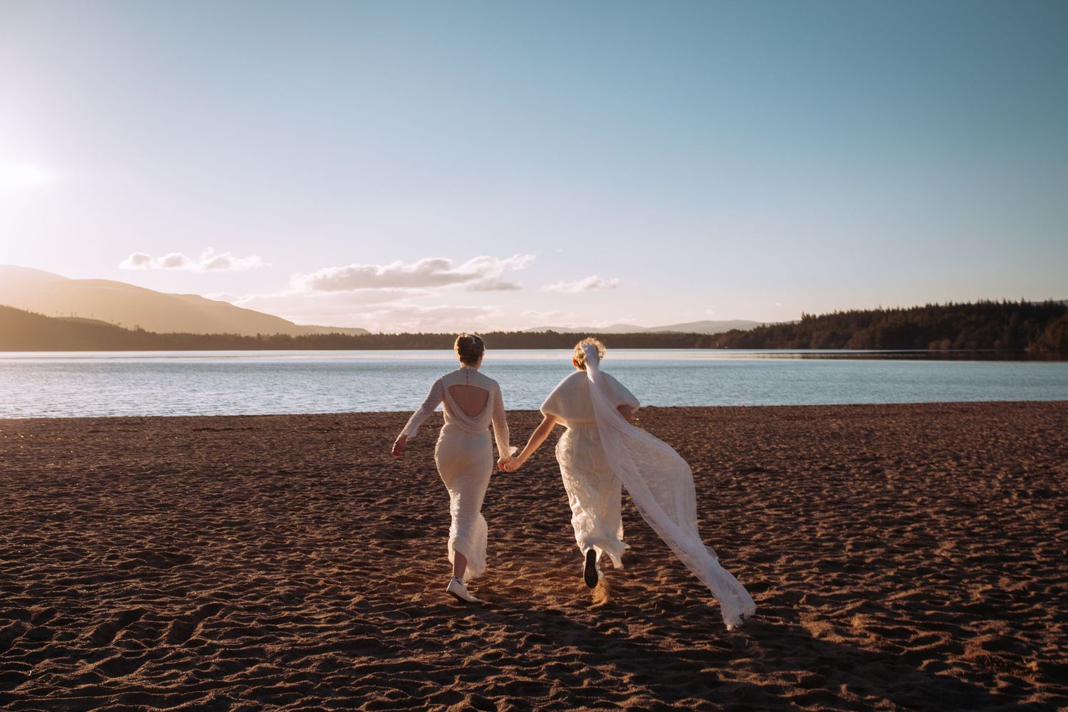 Silhouettes of a couple walking on a cracked desert landscape at sunset with mountains in the distance.