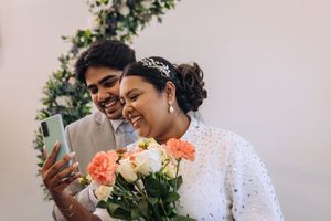 A couple in wedding attire share intimate moments while taking selfies with a phone during their celebration.