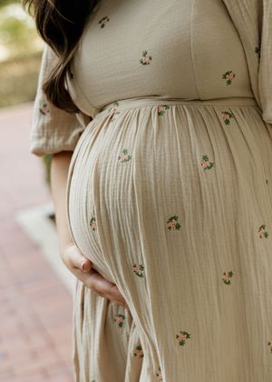 A series of photos showing a pregnant belly in a cream colored dress with small floral embroidery details.
