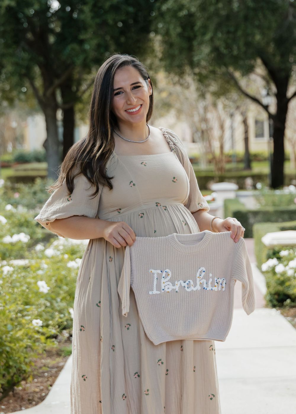 A cream-colored dress with floral embellishments is shown against an outdoor garden setting.