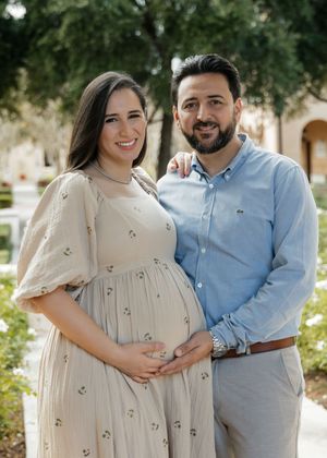 A couple stands together outdoors for maternity photos in coordinated cream and blue outfits.