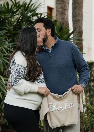 Couple in navy and white sweaters sharing a tender moment against a tropical garden backdrop.