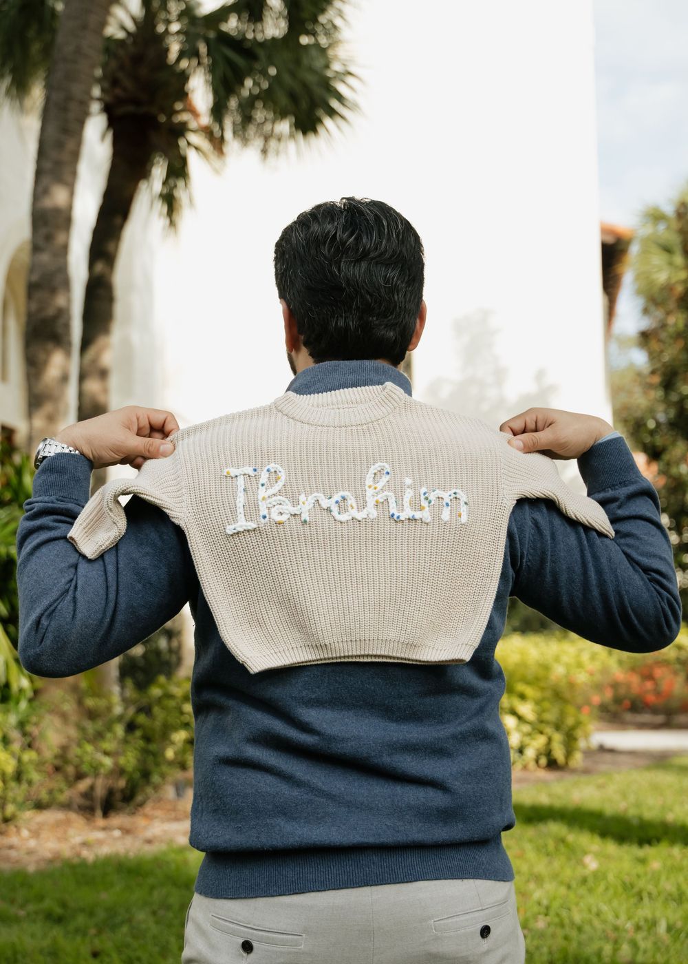 Back view of a person wearing a two-toned navy and cream sweater with text embroidered across the shoulders.