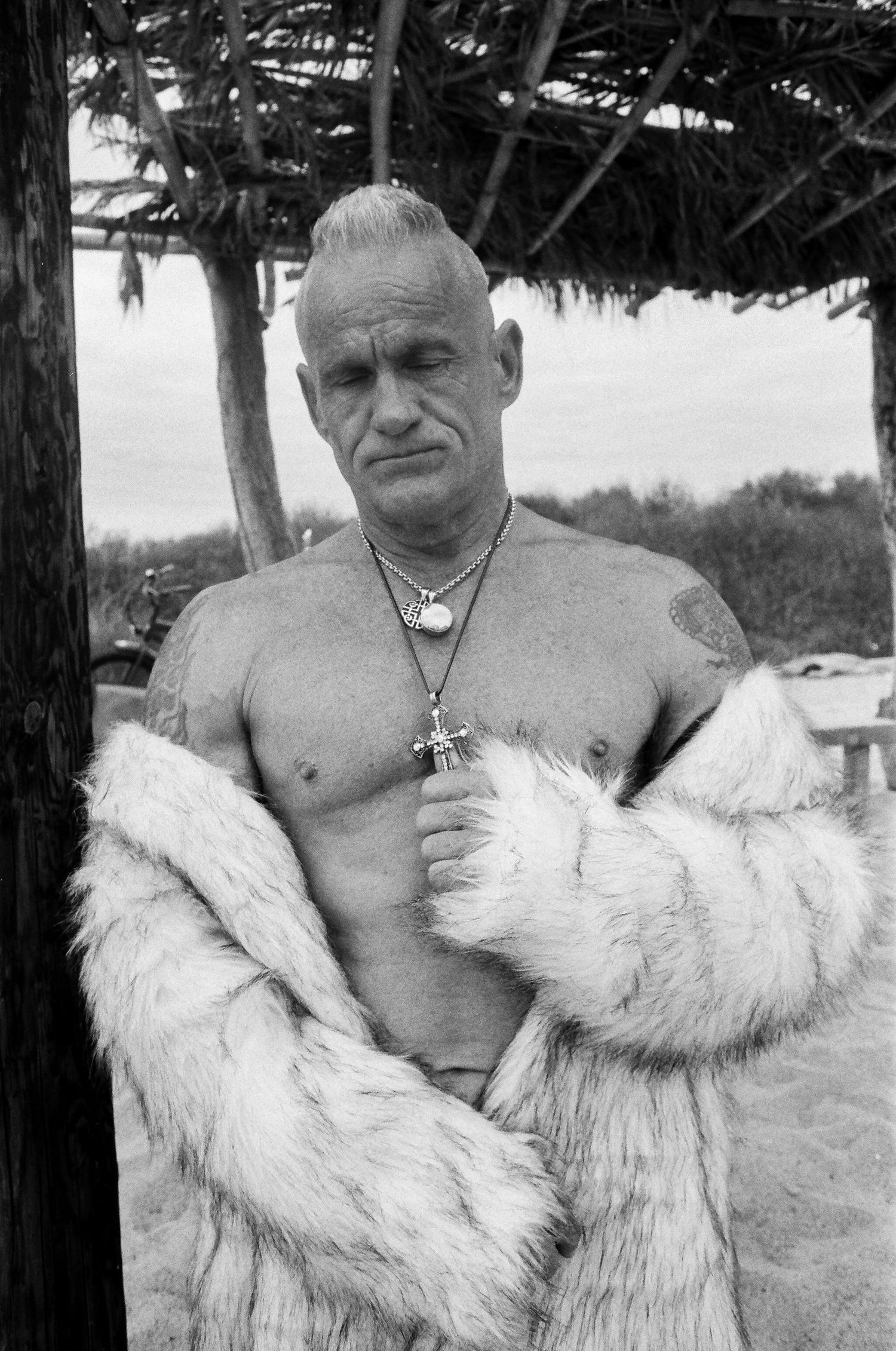 A figure stands on a beach wearing a white fur-like garment in a series of black and white photographs.
