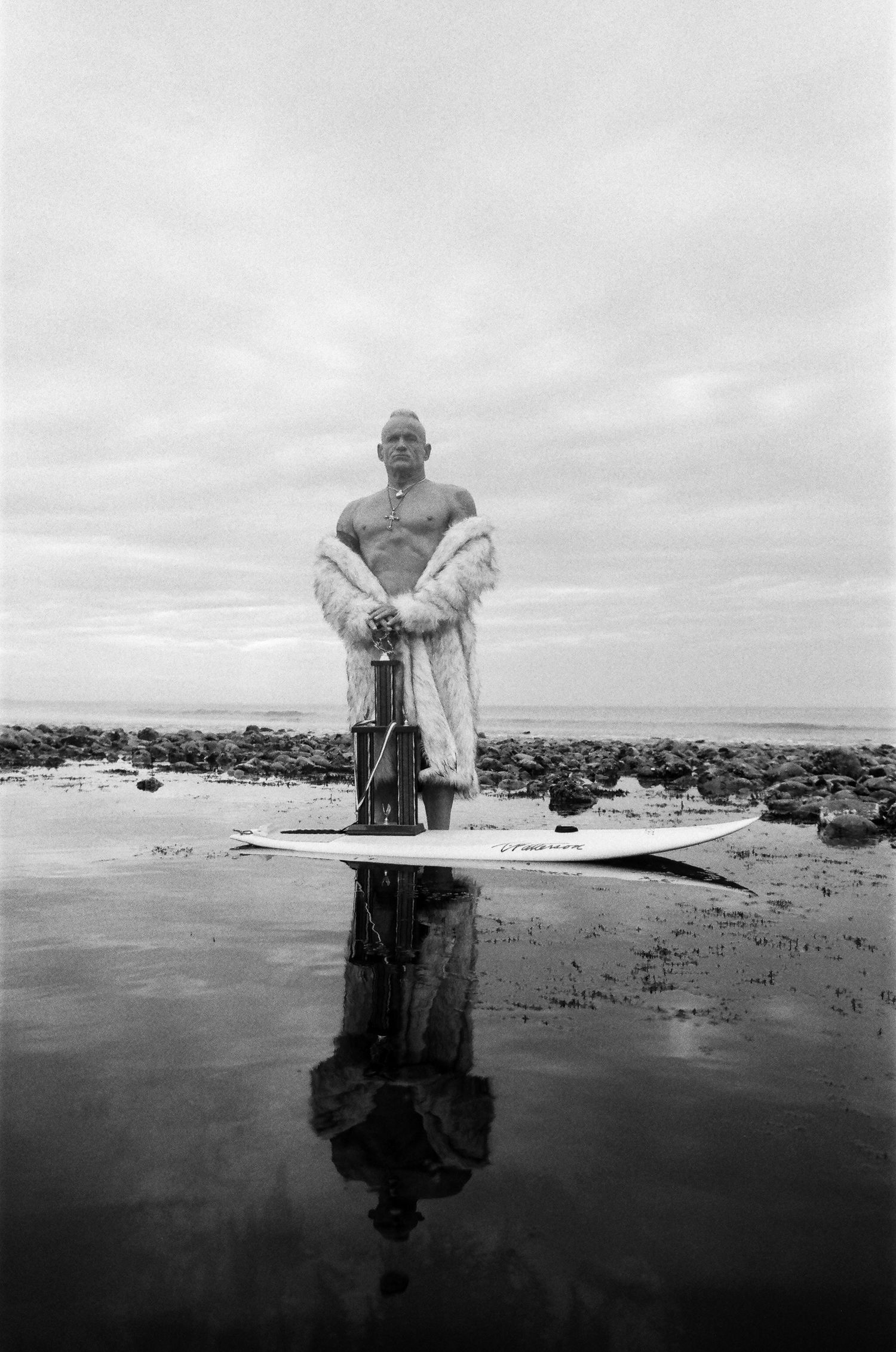 Black and white panoramic sequence shows a figure emerging from dark water against an overcast sky on a beach.