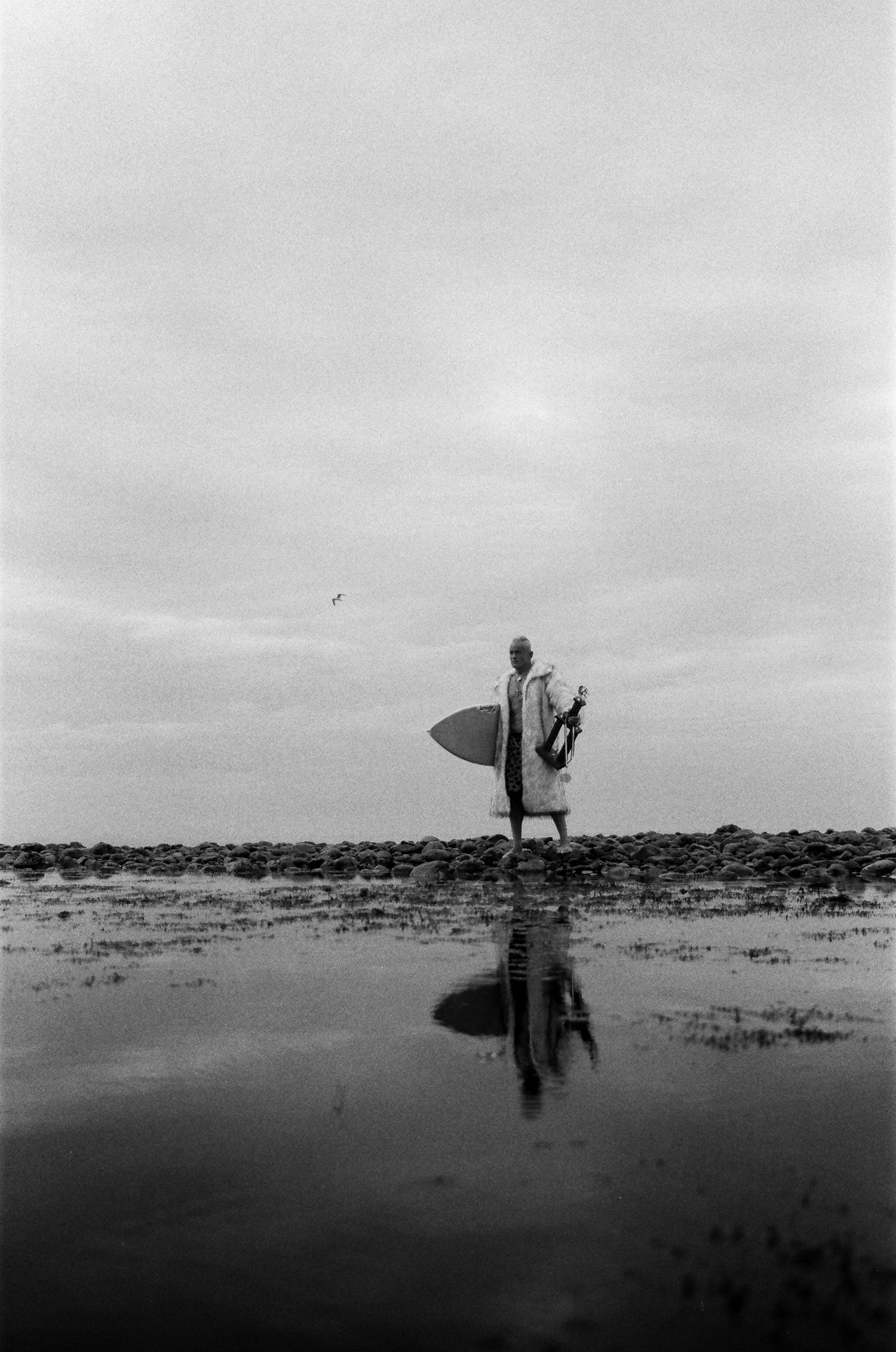 A silhouetted figure stands in shallow water against a cloudy sky in a minimalist black and white landscape.