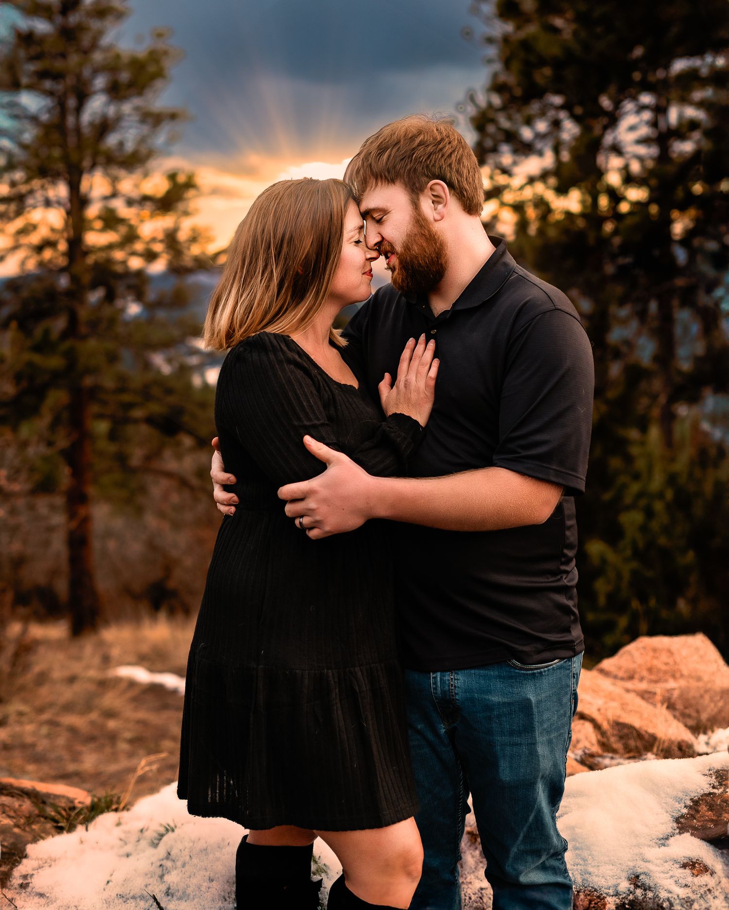 a couple embracing forehead to forehead while the sun shines from behind them on a Conifer, CO mountaintop