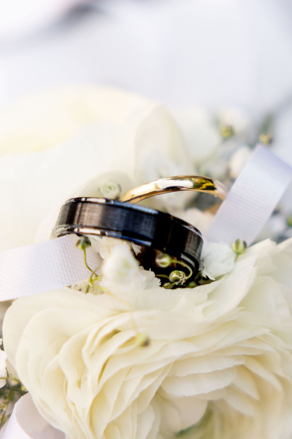 Wedding rings nestled in delicate white rose petals create an elegant macro photography composition.