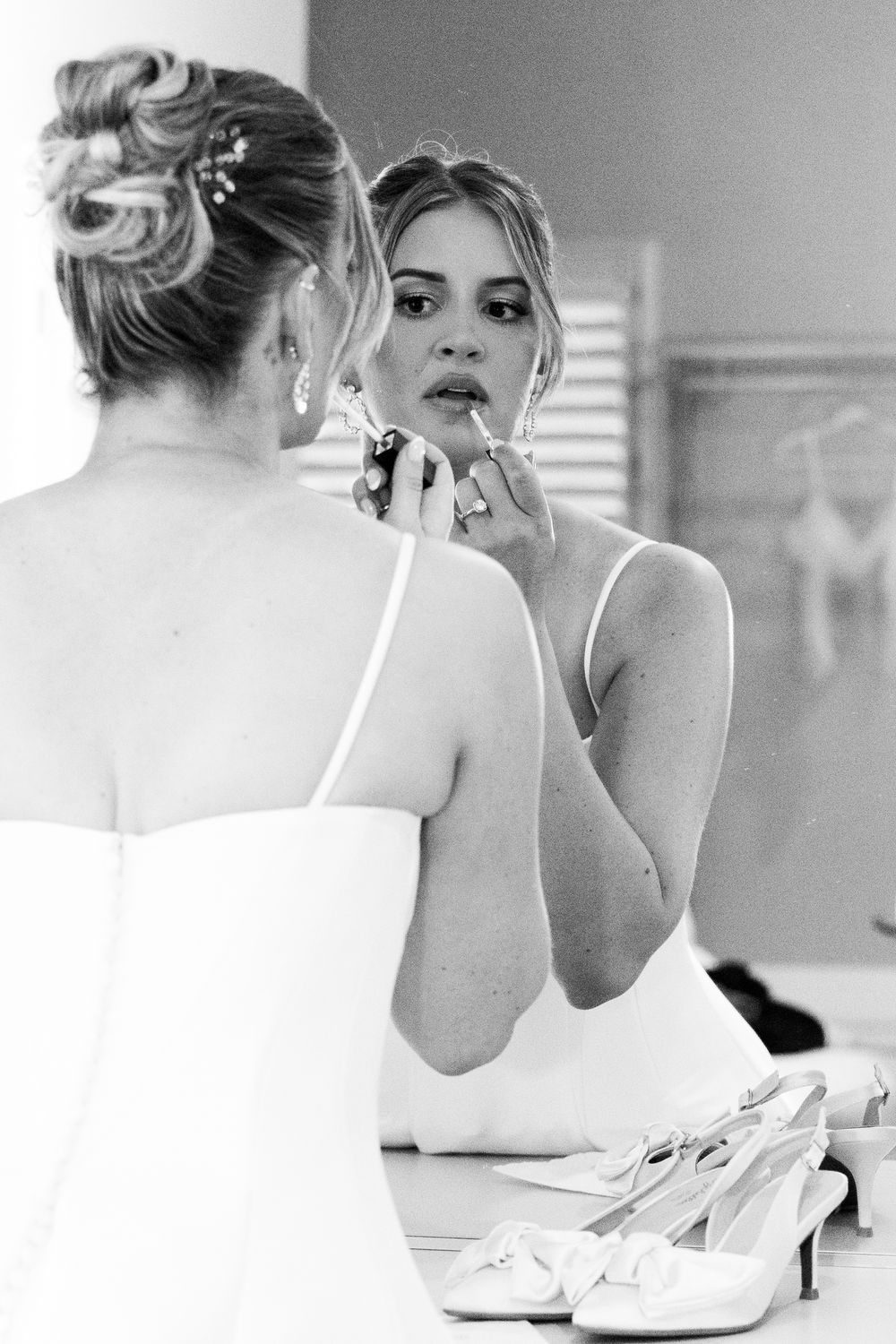 A black and white photo series showing someone applying makeup and getting ready in front of a mirror.