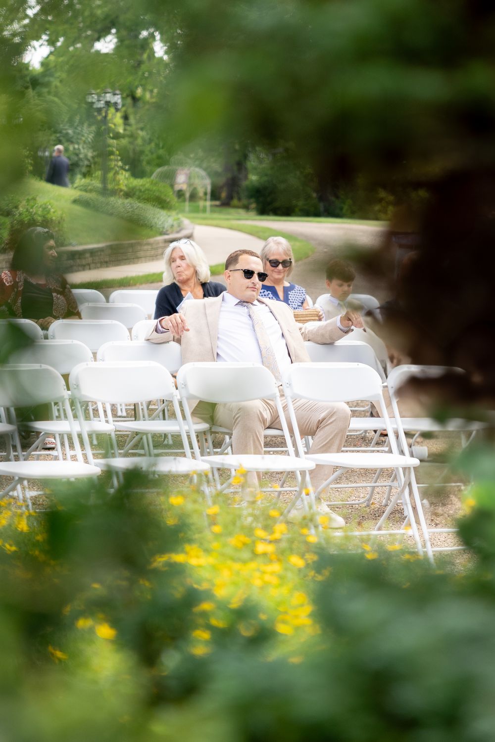 White folding chairs arranged outdoors for an event with yellow wildflowers and greenery in the foreground.