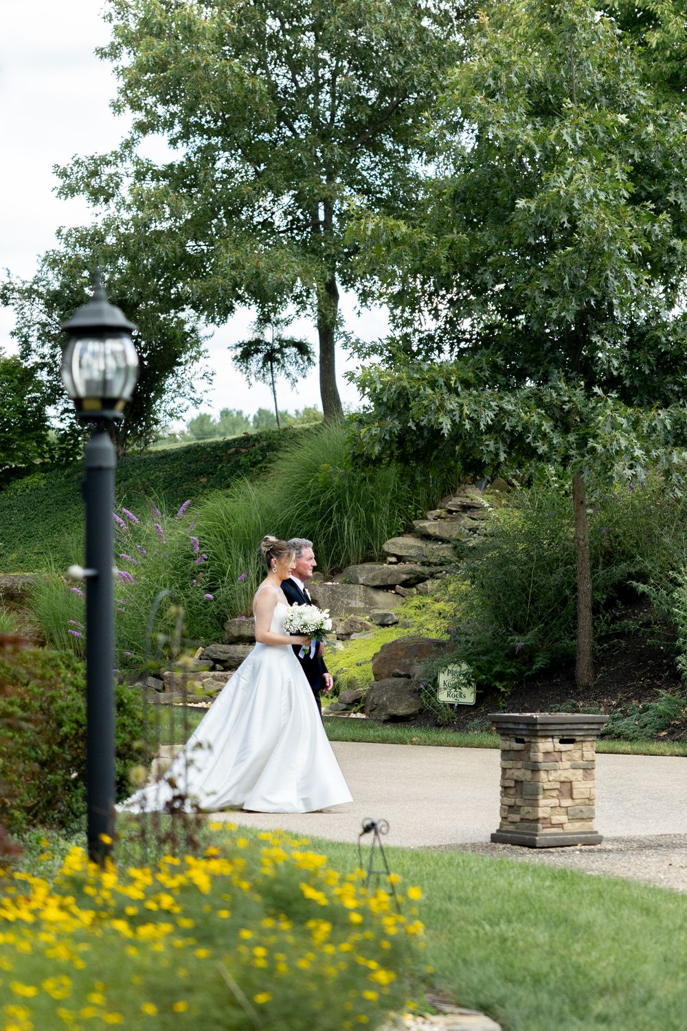 A couple shares a romantic moment on a garden bench surrounded by lush greenery and yellow wildflowers.