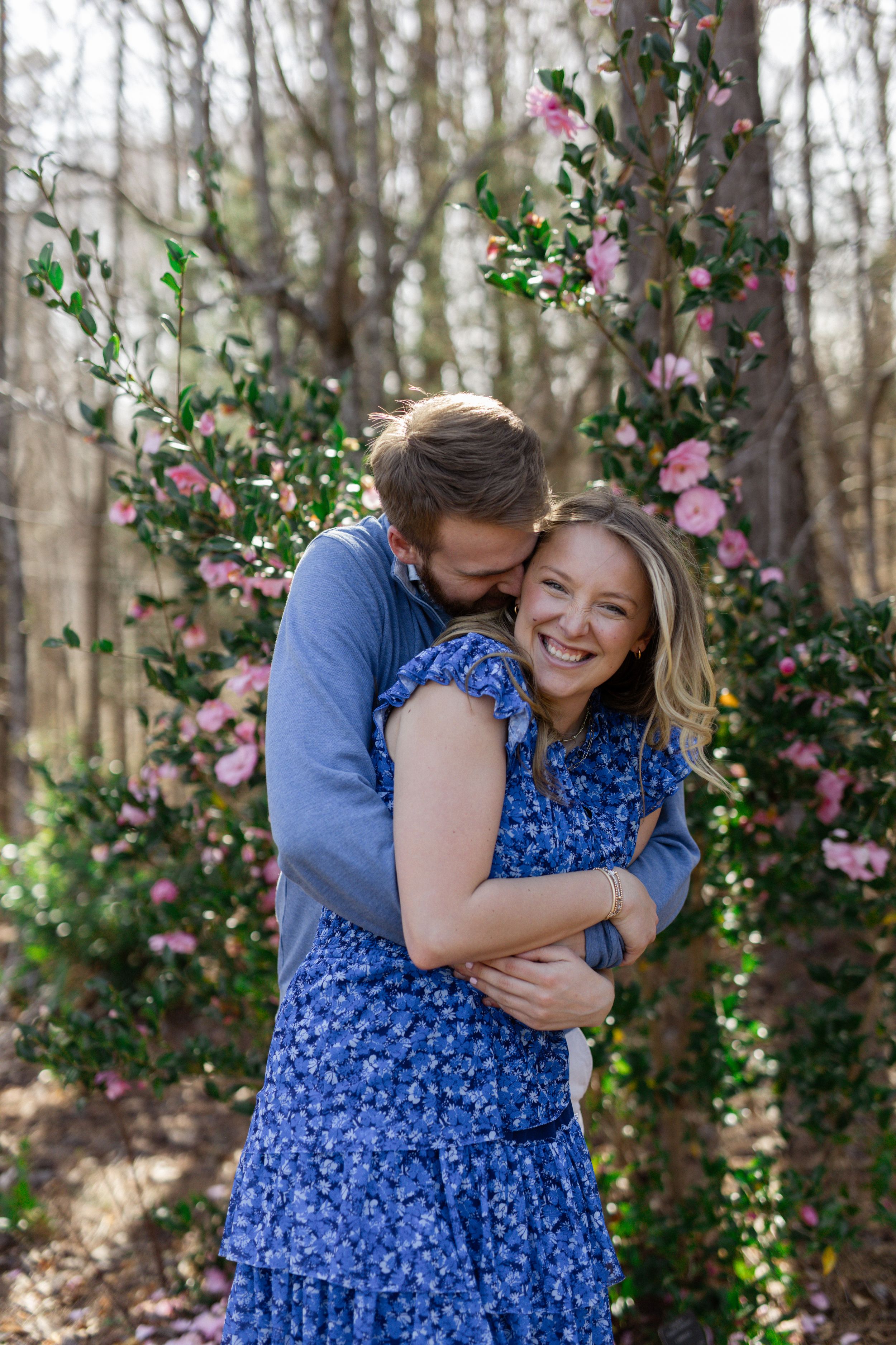 Couple embraces and laughs among spring flowers in blue coordinated outfits.