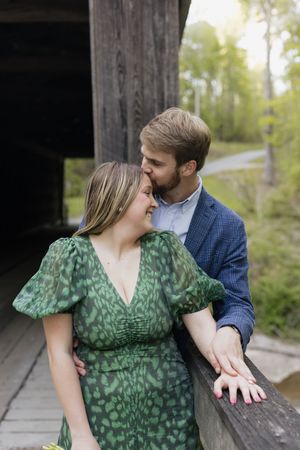 Couple shares a tender kiss on a wooden bridge, woman in green dress, man in blue blazer.