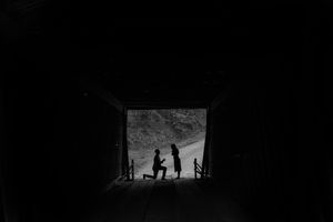 Silhouette of a marriage proposal inside a dark tunnel with light framing the romantic moment.
