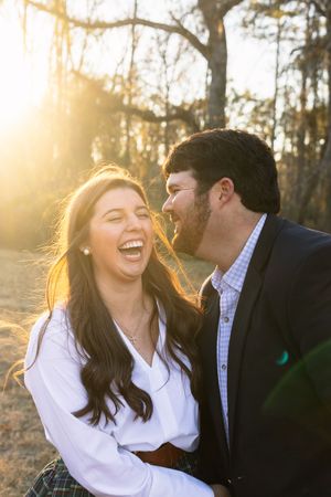 Couple laughs together during sunset engagement photo session in wooded area.