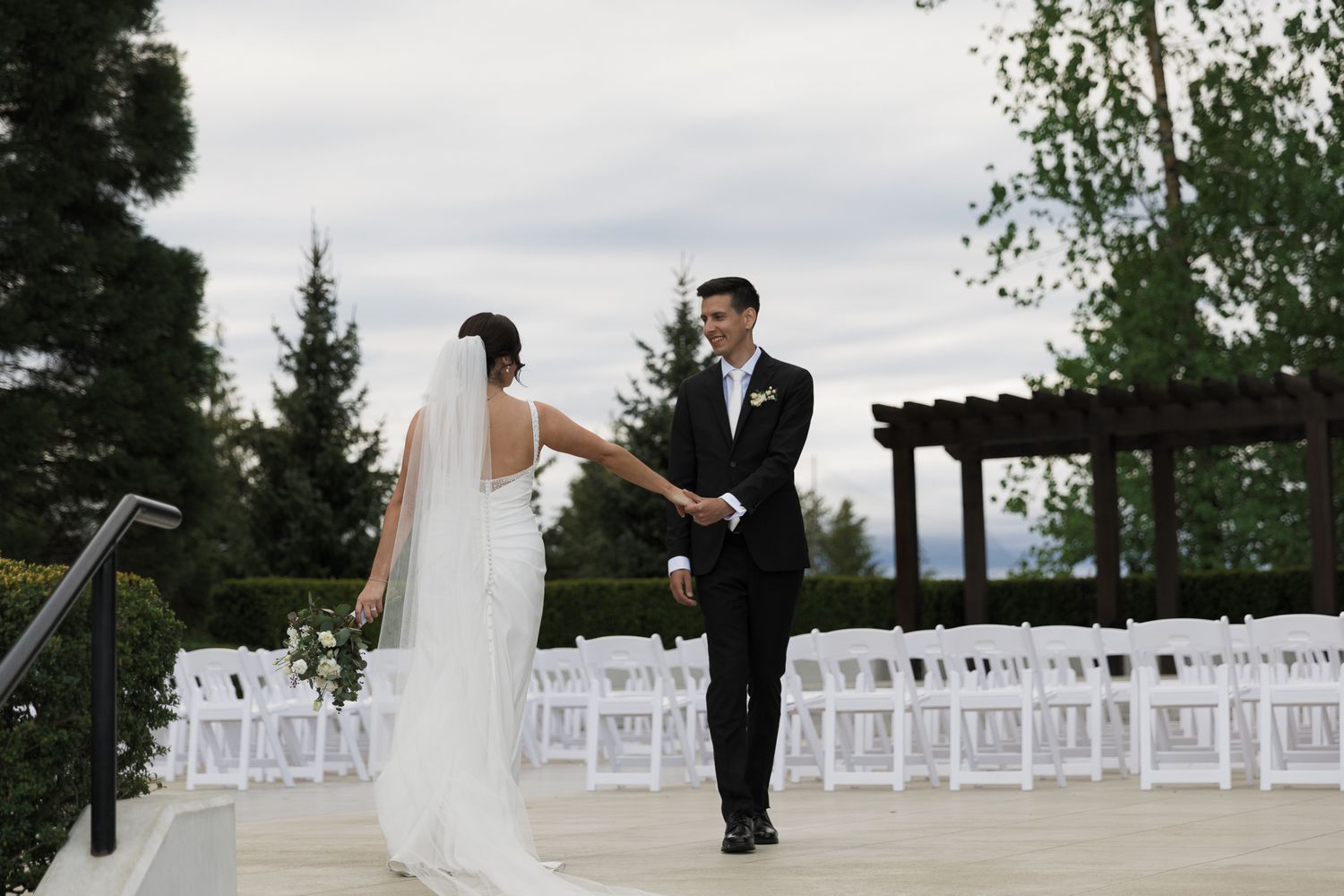 Bride and groom sharing a first look moment on outdoor wedding venue patio with white ceremony chairs.